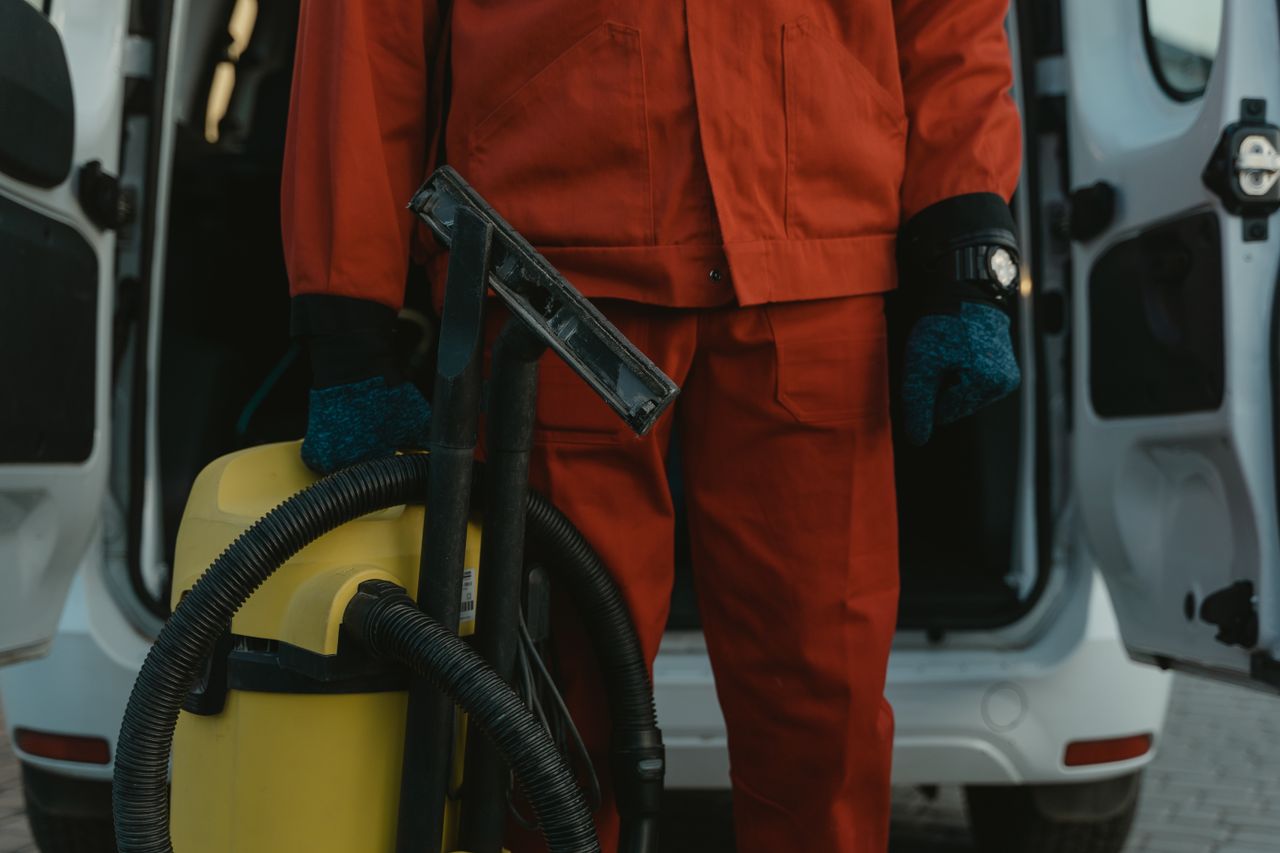 gallery-02 A professional cleaner in a red uniform holding a vacuum near a van, ready for service.